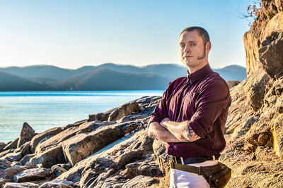 Young man standing on rock against sky