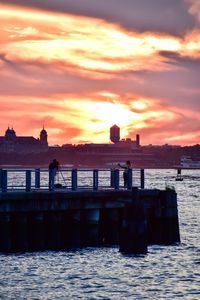 Promenade by sea in city against orange sky