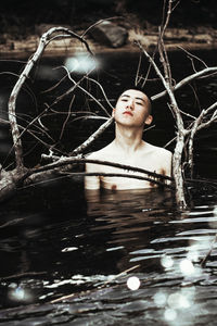 Shirtless man swimming in lake amidst branches