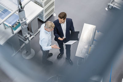 Two businessmen with clipboard talking in a factory