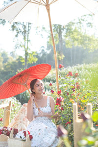 Young asian woman wearing a white dress poses with a rose in rose garden, chiang mai thailand