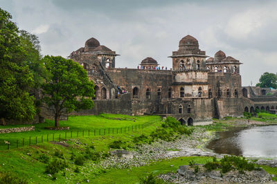 Jahaz mahal by pond against cloudy sky