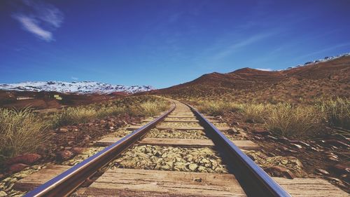 Railroad track by mountain against blue sky