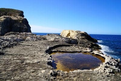 Rock formation on beach against clear blue sky