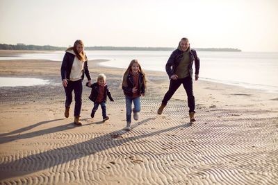 Family in a leather jacket run along the beach with their dog in autumn