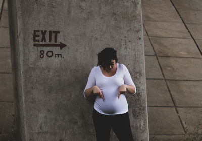Pregnant woman showing stomach while standing against wall