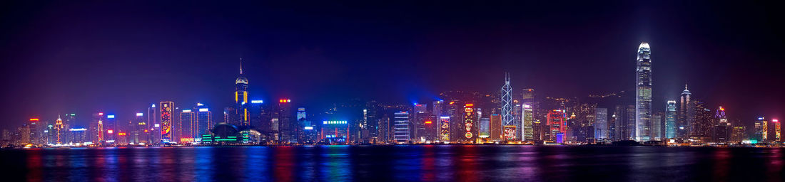 Panoramic shot of illuminated cityscape by river at night