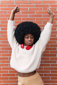 Young woman with arms raised standing against brick wall