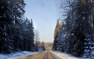 Empty road amidst snow covered trees against sky