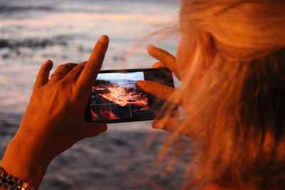 Close-up of woman photographing sea with mobile phone during sunset