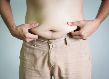 Midsection of man holding belly against gray background