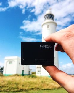 Close-up of hand holding camera against the sky