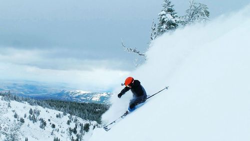 Person skiing on snowcapped mountain against cloudy sky