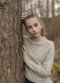 Portrait of teenage girl standing behind tree in forest