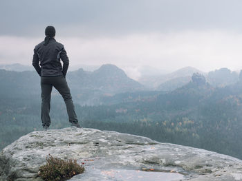 Rear view of man standing on mountain against sky