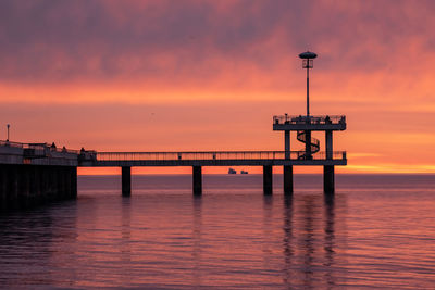 Pier over sea against dramatic sky during sunset