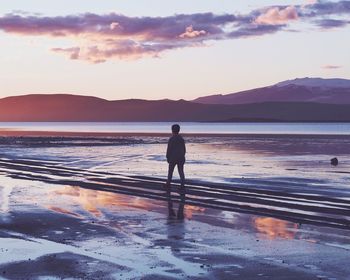 Rear view of silhouette man standing at beach against sky