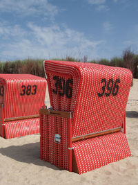 Hooded chairs at beach against sky