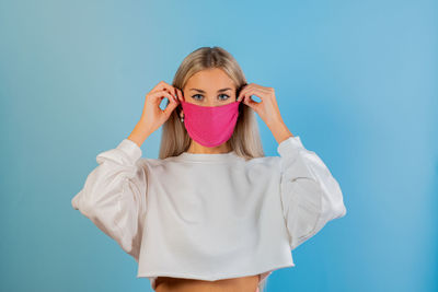 Portrait of beautiful young woman wearing mask against blue background