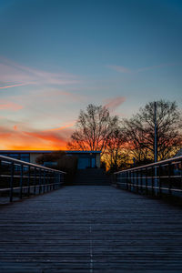 Pier over river against sky during sunset