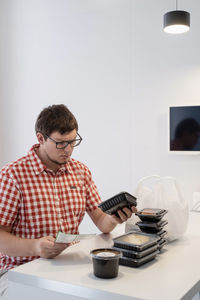 Full length of man holding camera while sitting on table