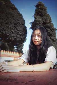 Portrait of a smiling young woman sitting against trees