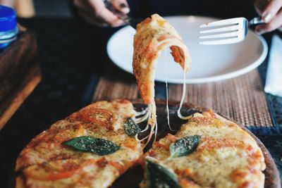 Close-up of hands holding pizza with fork and knife on table