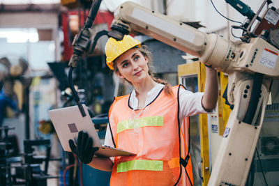 Young engineer examining machinery while holding laptop at factory