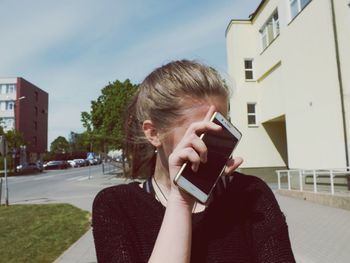 Young woman using mobile phone in city against sky