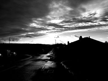 Road by silhouette city against sky at sunset