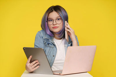 Young woman using laptop while sitting on yellow background