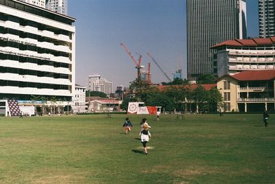 People playing on field against buildings in city