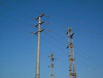 Low angle view of electricity pylon against blue sky