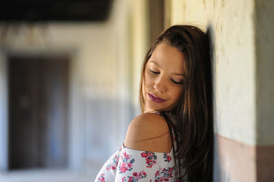 Young woman looking down while standing against wall