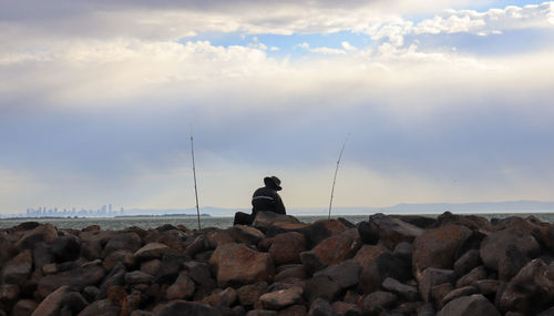 Man sitting on rocks by sea against sky