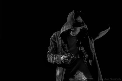 Man holding gun while wearing hooded shirt against black background