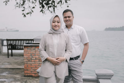 Portrait of smiling couple standing against sea