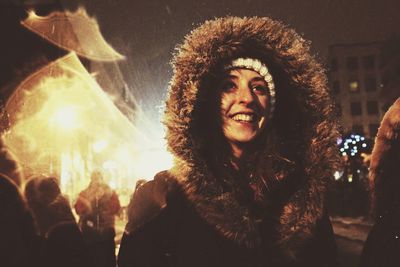Cheerful woman wearing fur hood in city at night