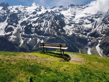 Bench on field overlooking snow covered mountains