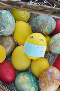 Basket with colorful eggs and a yellow egg with protection mask