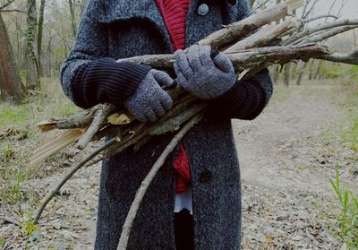 Midsection of woman in warm clothing holding wood at field