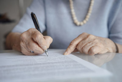 Hands of senior woman writing on paper with pen