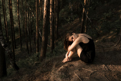 Woman sitting against trees in forest