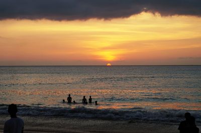 Silhouette people on beach against sky during sunset