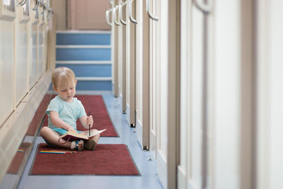 A little toddler baby boy sits on the floor of a train car and draws with colored pencils. 