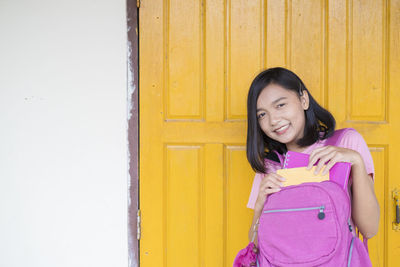 Portrait of a smiling girl standing against yellow wall