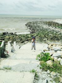 Boy standing on staircase by sea against sky