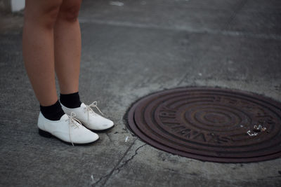 Low section of woman standing by manhole