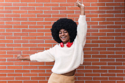 Young woman with arms raised standing against brick wall