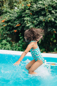 Diverse mixed race toddler girl at home having fun in kiddie pool in backyard being very happy